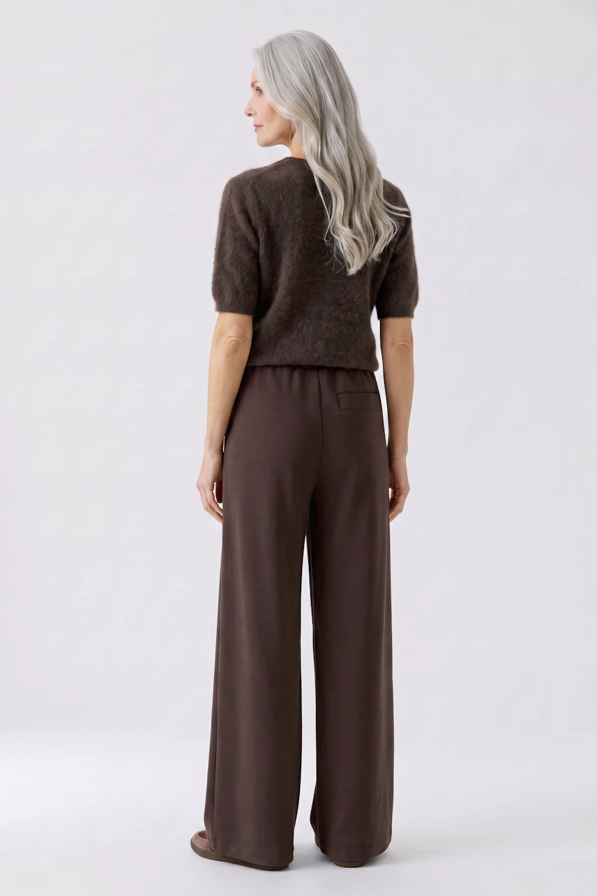 Woman in brown Marlene trousers and fuzzy pullover, standing confidently with long gray hair.