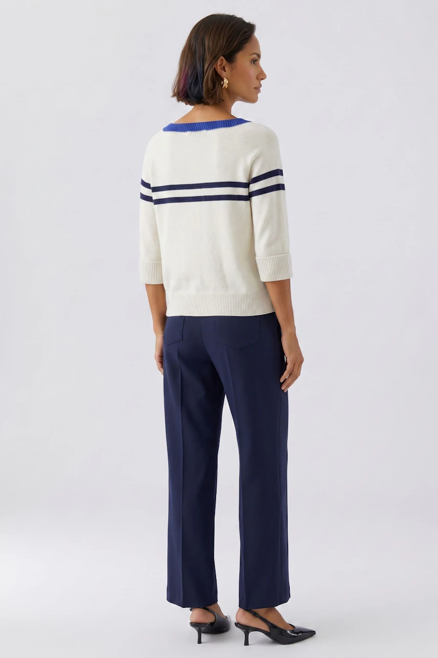 Casual women's pullover: Woman in a white pullover with navy stripes, paired with navy pants, stands confidently.