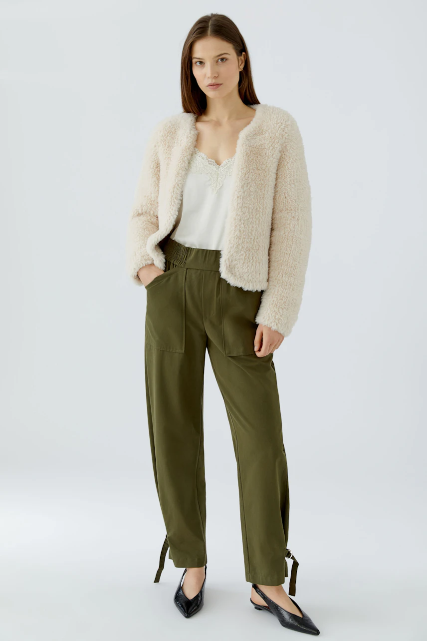 Frau in flauschiger Strickjacke, weißem Top und olivgrüner Hose. Lässig und modern.