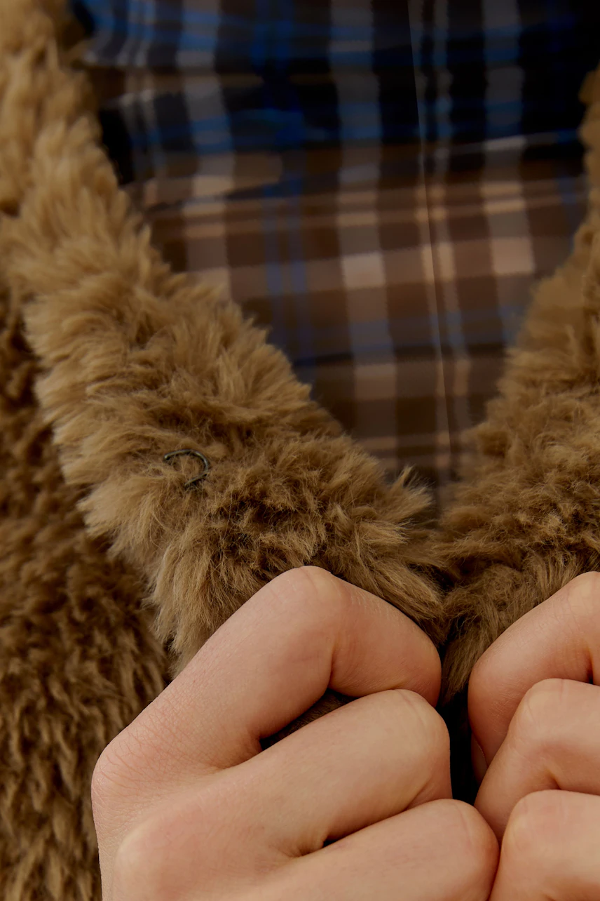 Cozy knit vest: Woman in a fluffy brown knit vest over a plaid shirt, holding the vest's collar.