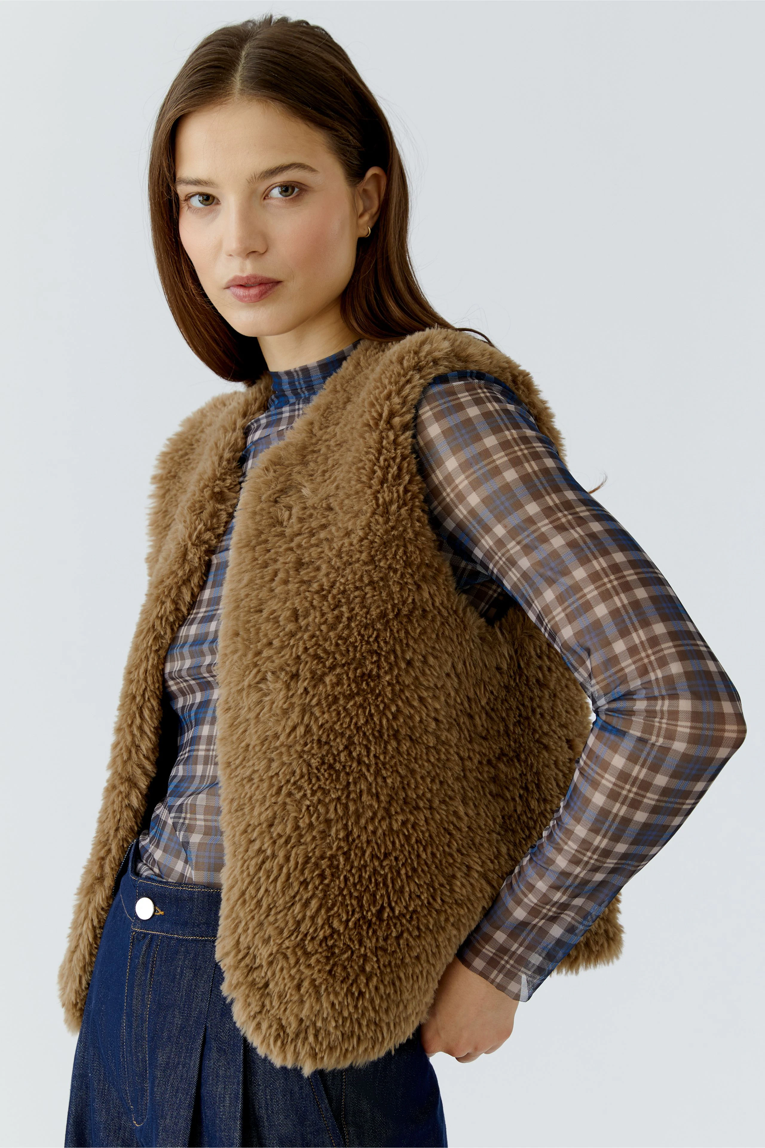 Woman in a brown knit vest over a plaid shirt, paired with dark jeans, looking confidently to the side.