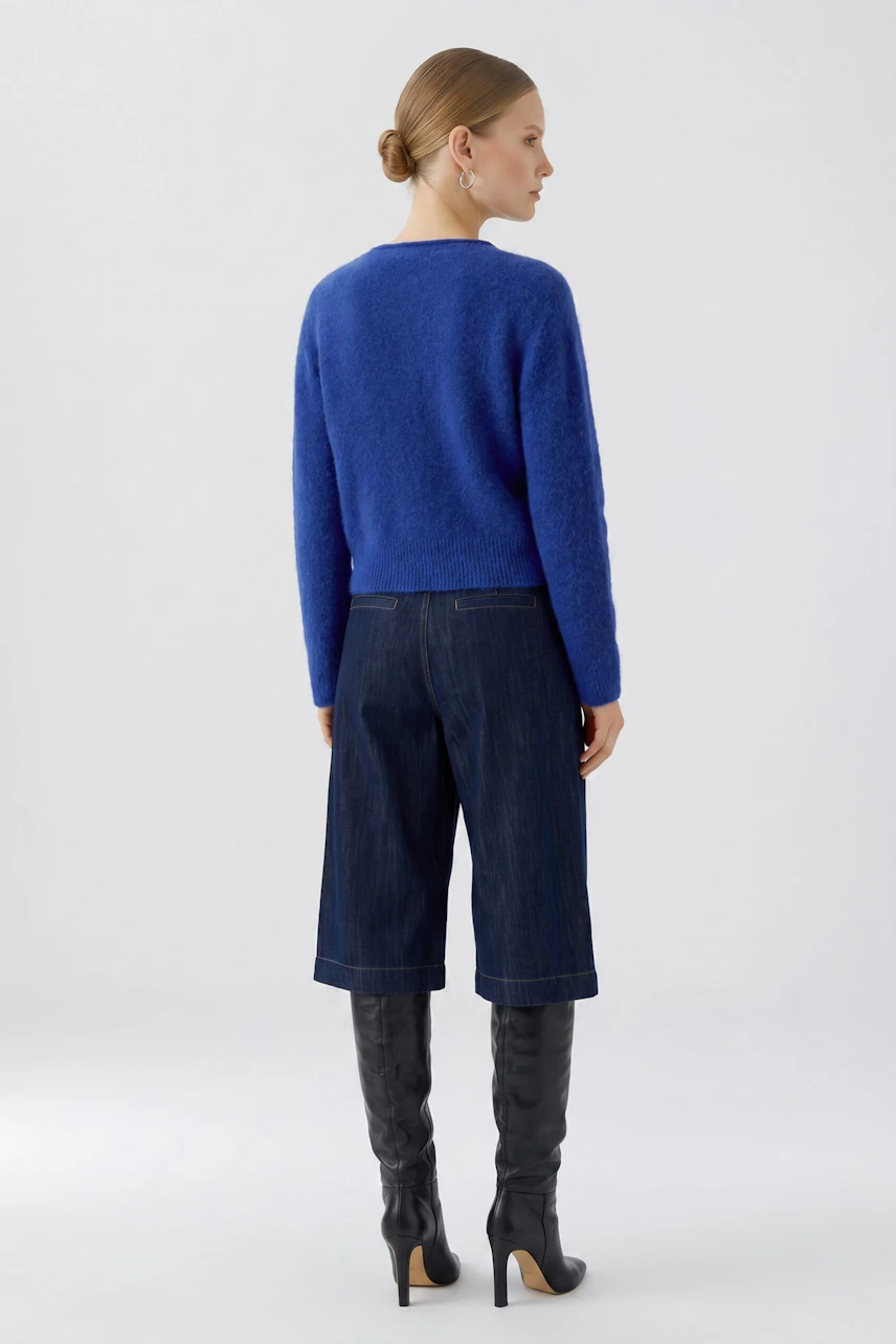 Blue knit cardigan: Woman in a vibrant blue cardigan, denim culottes, and knee-high black boots.
