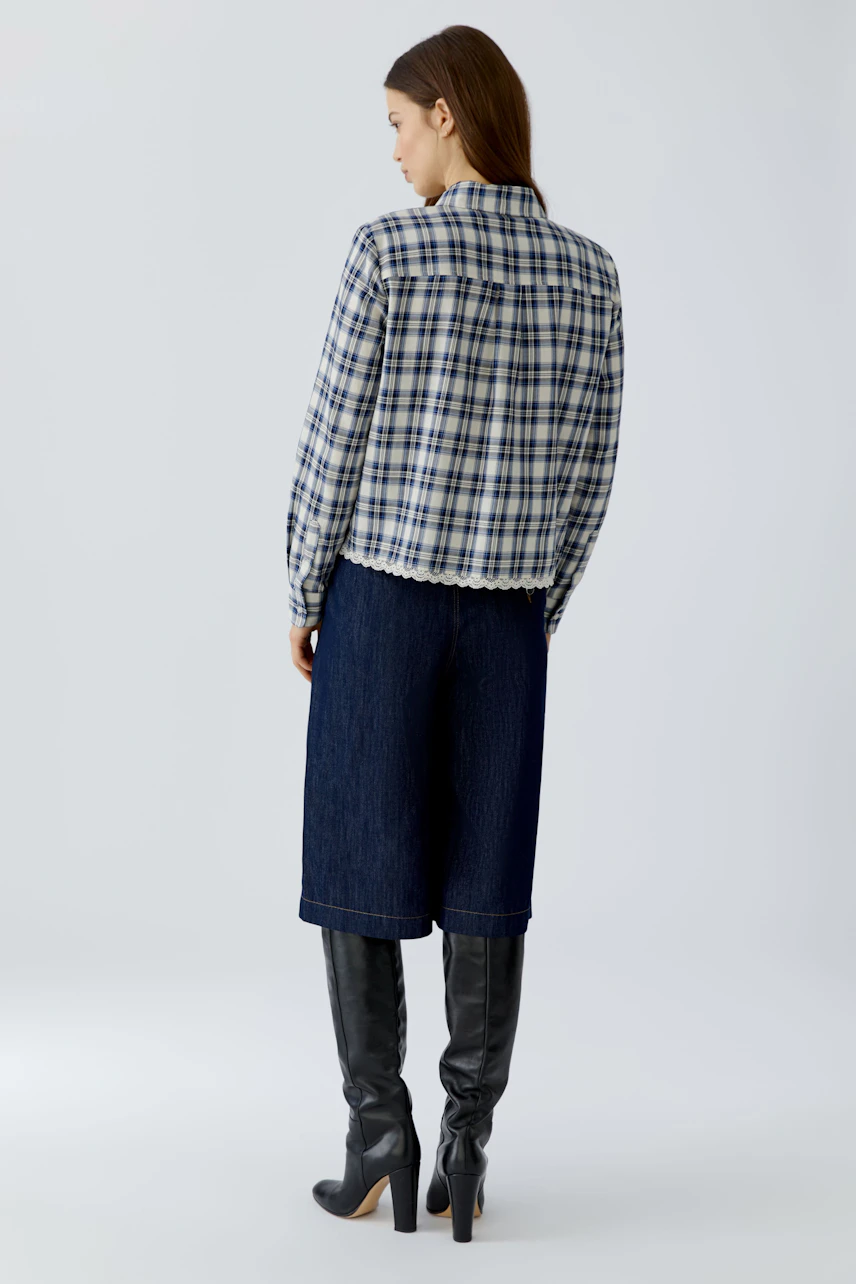 Kariertes Hemdbluse: Frau in karierter Bluse und dunkler Jeans, blickt zur Seite. Lässiger, moderner Look.