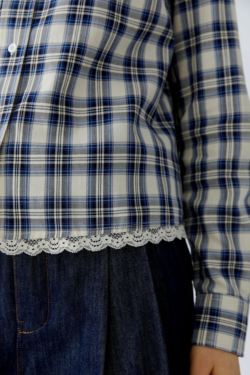 Kariertes Hemdbluse: Frau in blau-weißem Karohemd mit Spitzenbesatz, kombiniert mit dunkler Jeans.