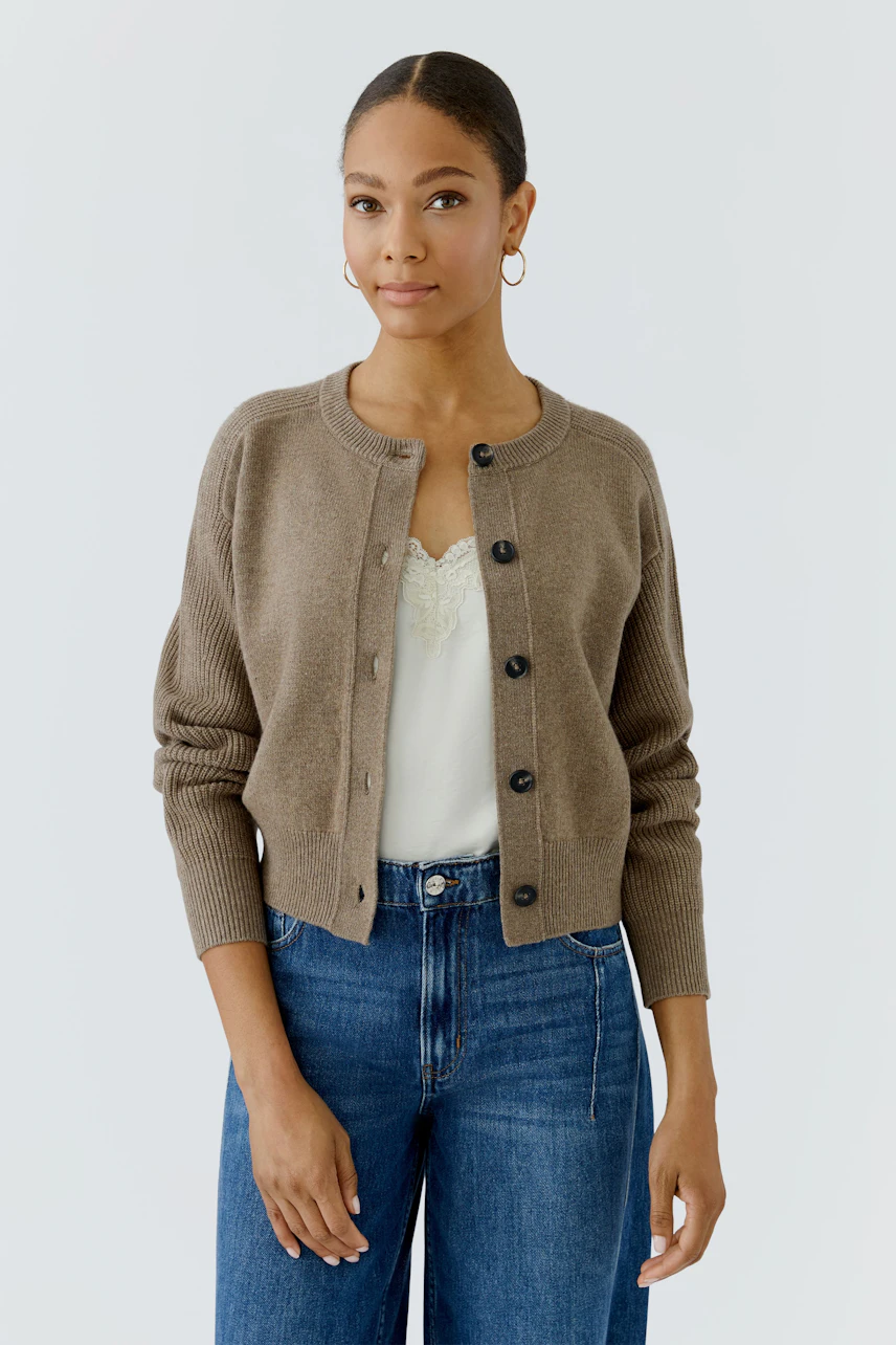 Casual cardigan: Woman in a brown button-up cardigan over a white top and blue jeans, looking relaxed.