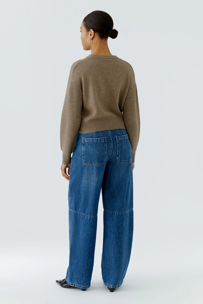 Casual cardigan: Woman in a brown knit cardigan and wide-leg jeans, viewed from the back.
