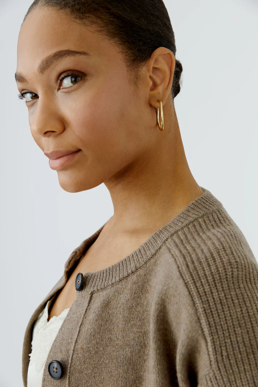 Woman in a cozy cardigan: Brown knit cardigan with button details, worn by a woman with gold hoop earrings.