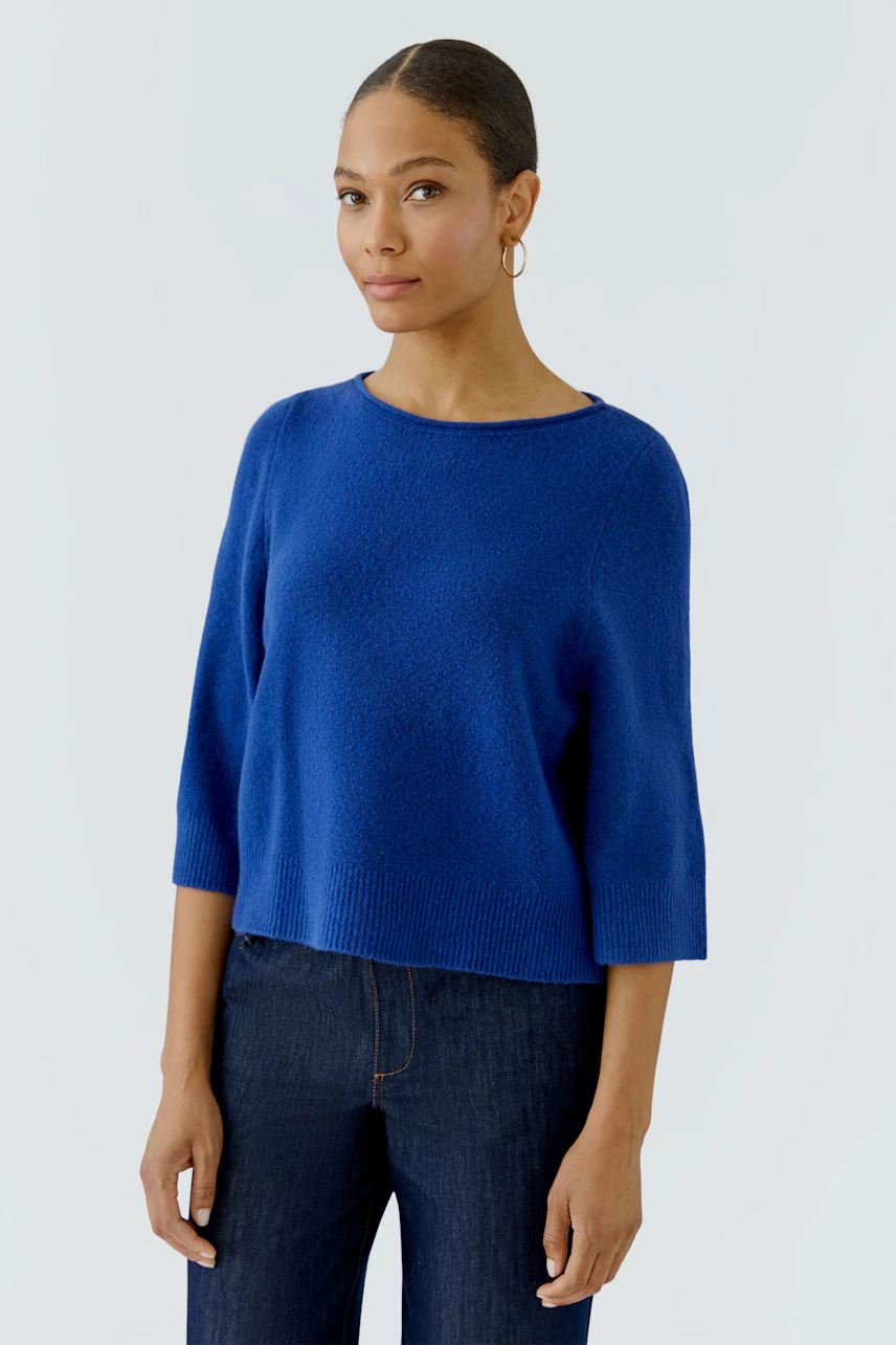 Casual women's pullover: Woman in a blue pullover with 3/4 sleeves and dark jeans, looking relaxed.