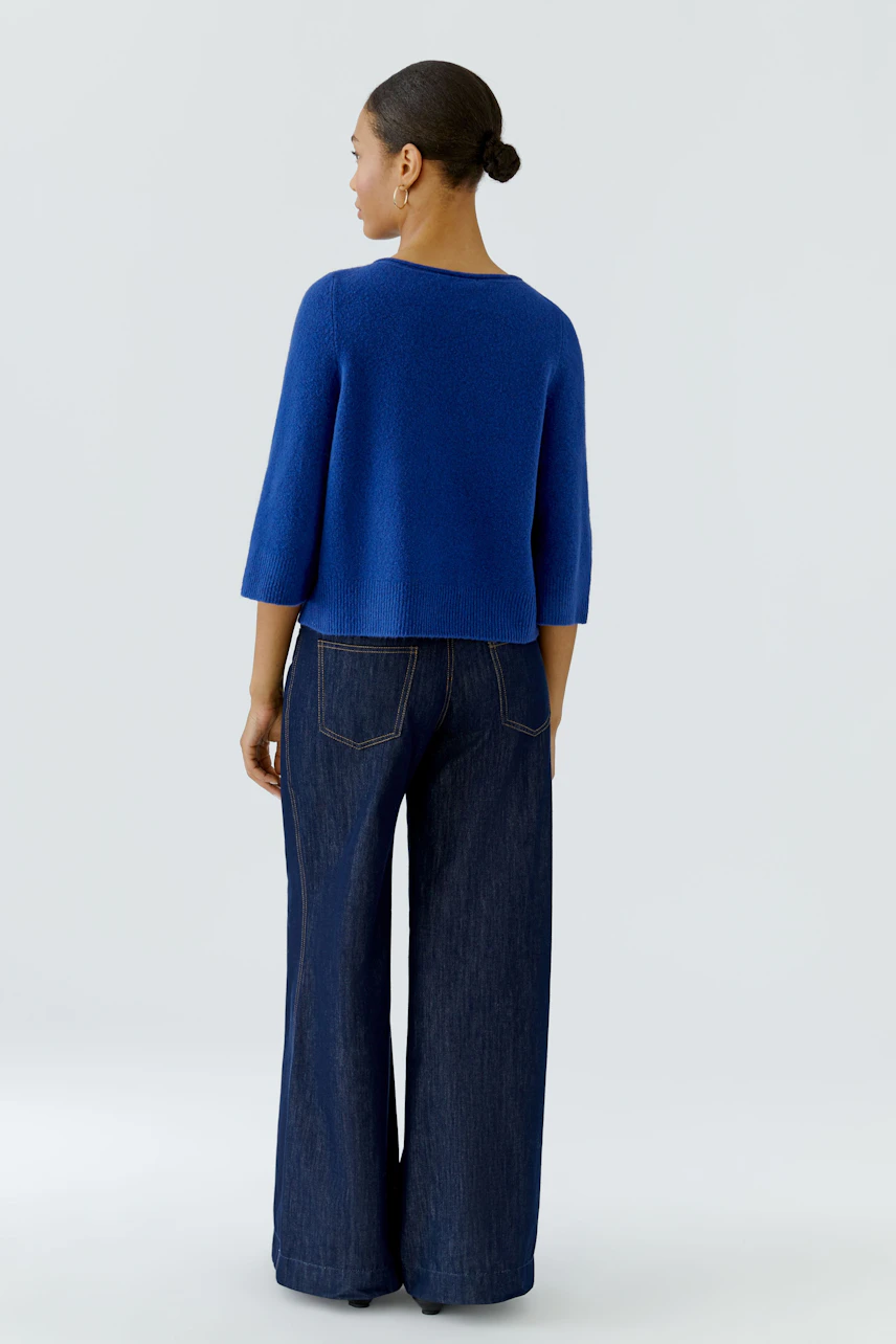 Casual pullover: Woman in a blue pullover with wide-leg jeans, viewed from the back.