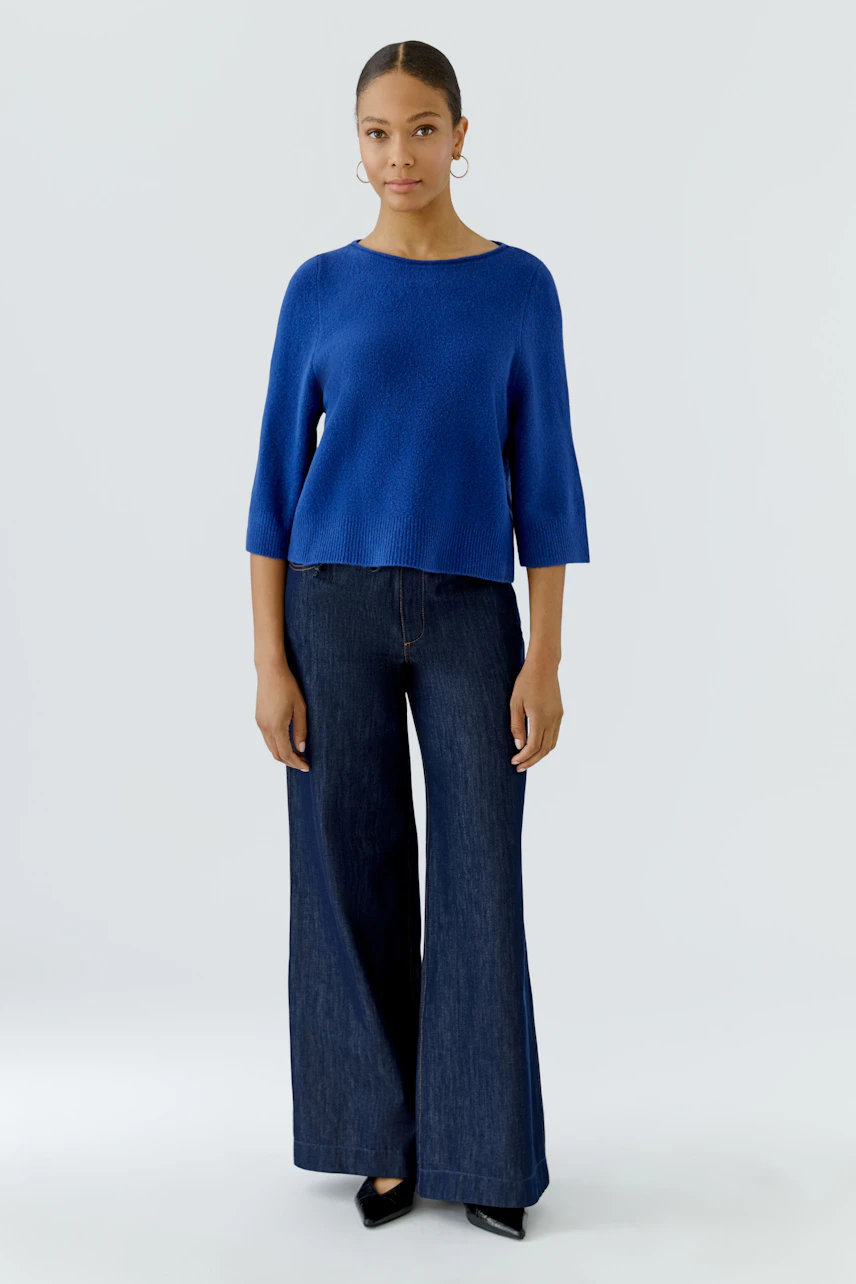 Casual women's pullover: Woman in a blue pullover and wide-leg jeans stands confidently.