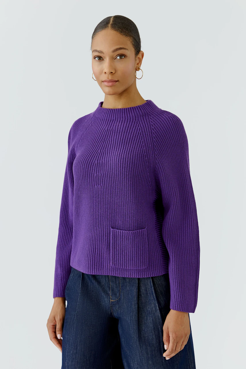 Frau im lila Pullover mit Rundhalsausschnitt und Tasche, kombiniert mit dunkler Jeans.