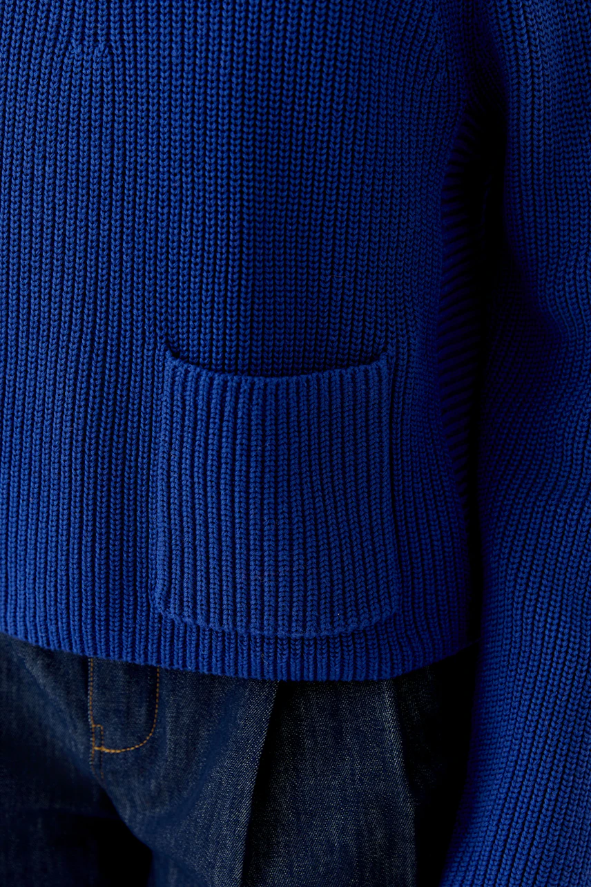 Blue ribbed pullover with pocket detail, paired with dark denim jeans. Casual and stylish look.