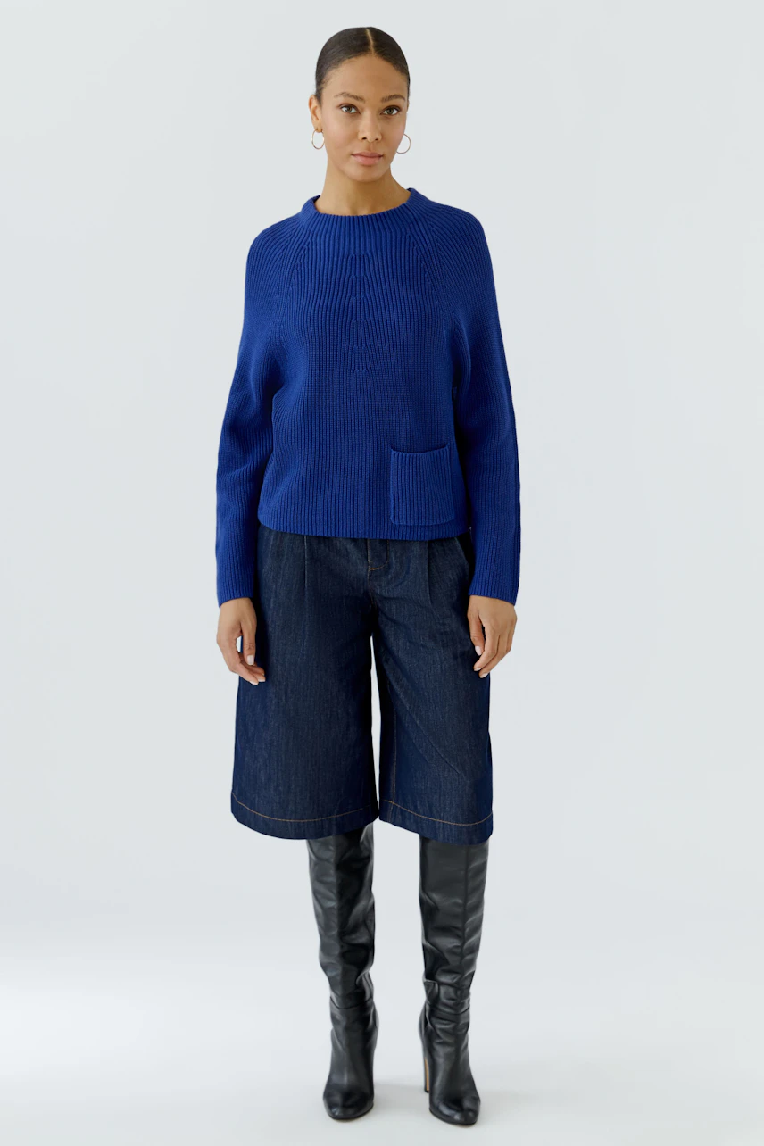 Casual women's pullover: Woman in blue pullover with pocket, denim culottes, and knee-high black boots.