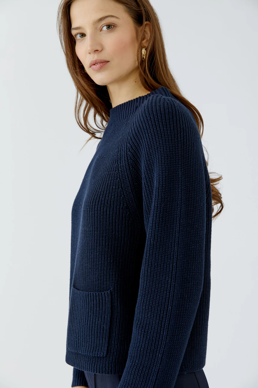 Woman in a navy pullover with a front pocket, looking to the side. Casual and stylish design.