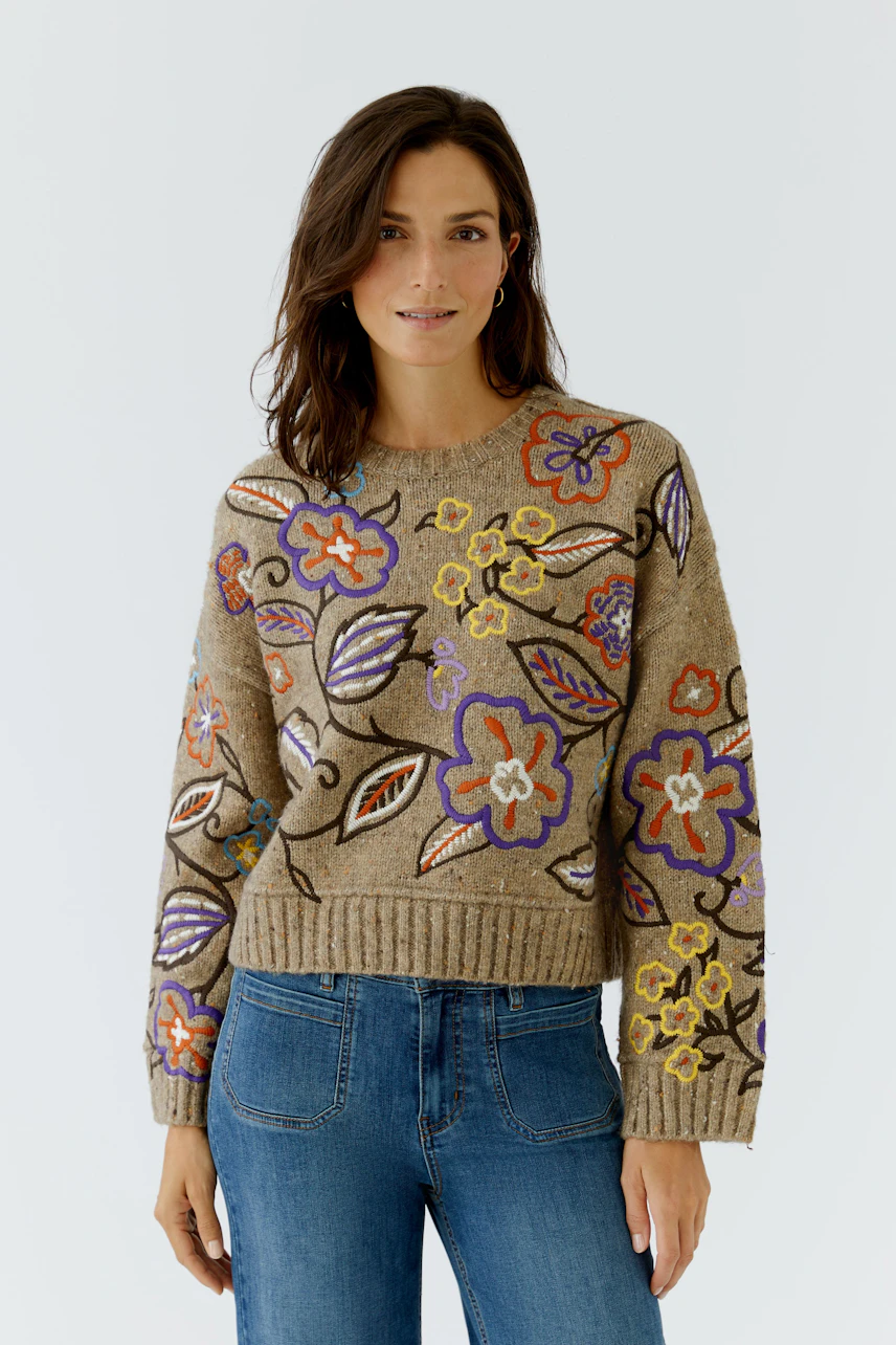 Frau im floralen Pullover: Lächelnde Frau trägt bunten Pullover mit Blumenmuster und blaue Jeans.