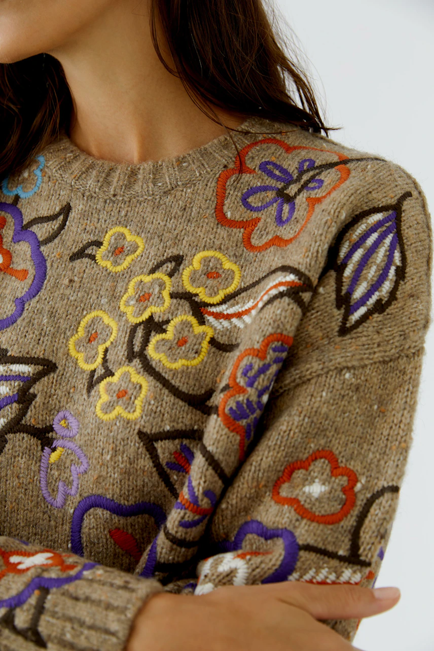 Pullover mit buntem Blumenmuster auf beigem Hintergrund. Ideal für einen farbenfrohen Look.