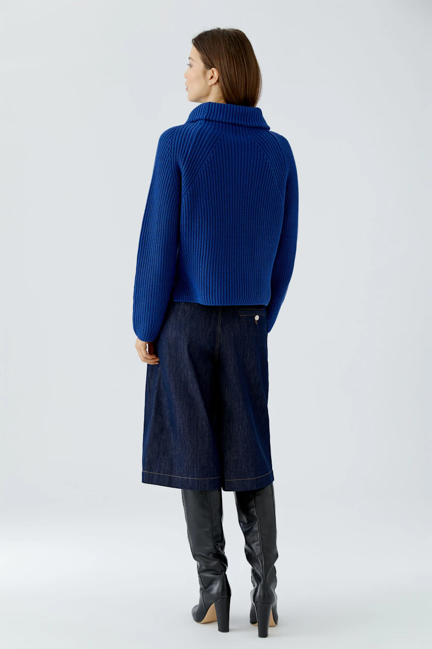 Woman in blue pullover, wide-leg jeans, and knee-high boots, viewed from the back.