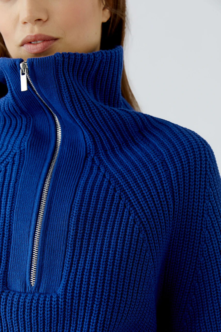 Woman in a blue ribbed pullover with a high collar and front zipper, showcasing a casual style.