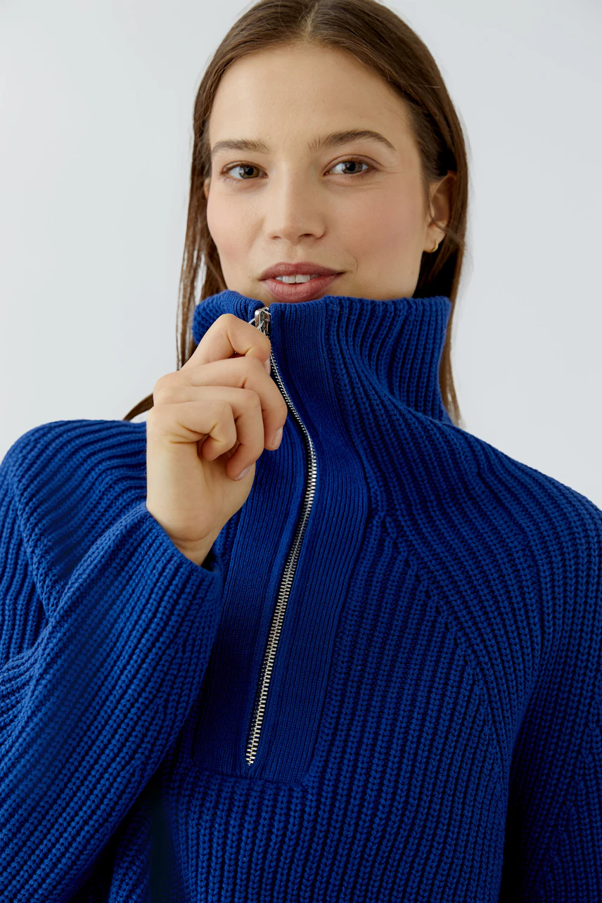 Woman in a vibrant blue pullover with a high collar and zipper, exuding a casual and confident style.