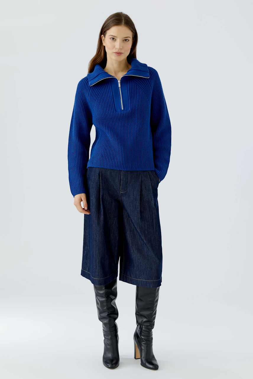 Woman in a blue pullover with a zip collar, paired with wide denim pants and black boots.