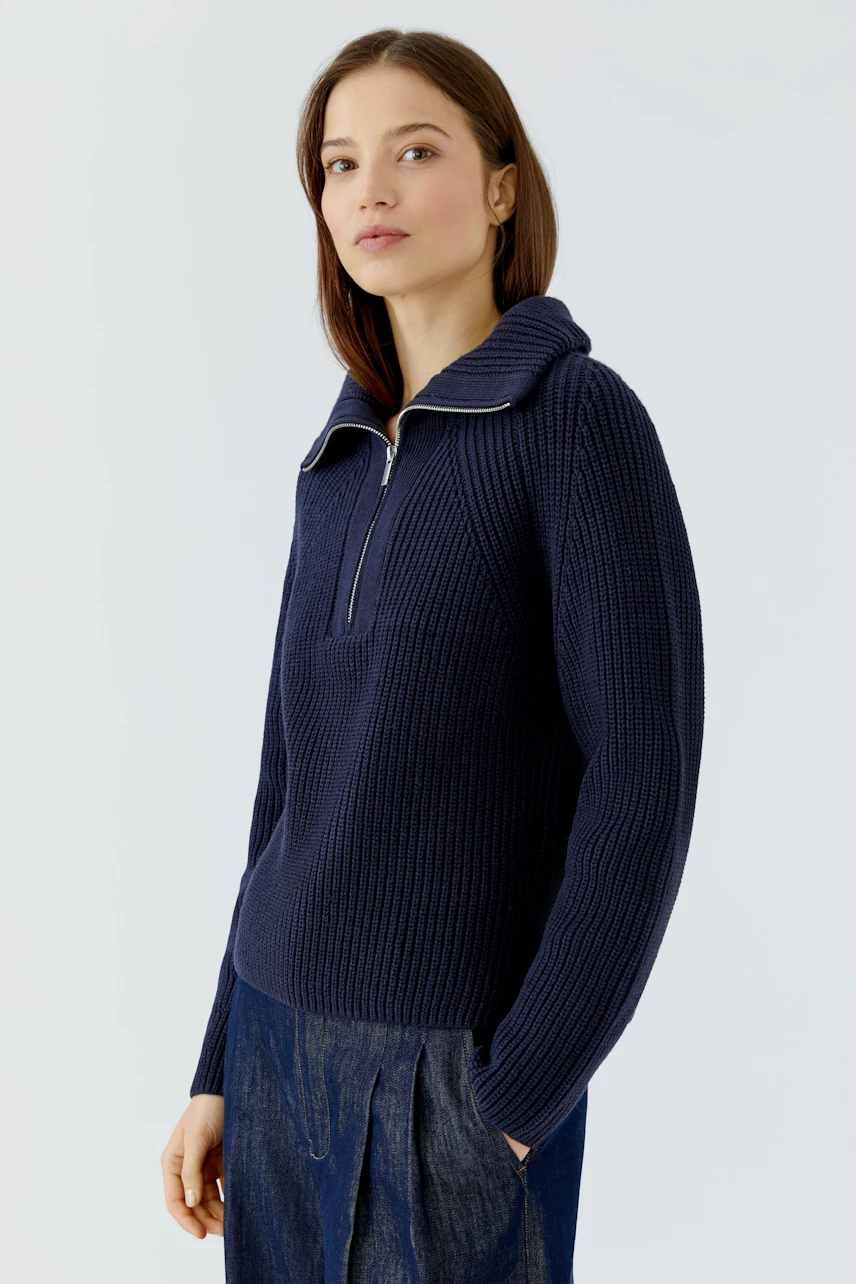 Casual women's pullover: Woman in navy knit pullover with zip collar, paired with dark denim skirt.