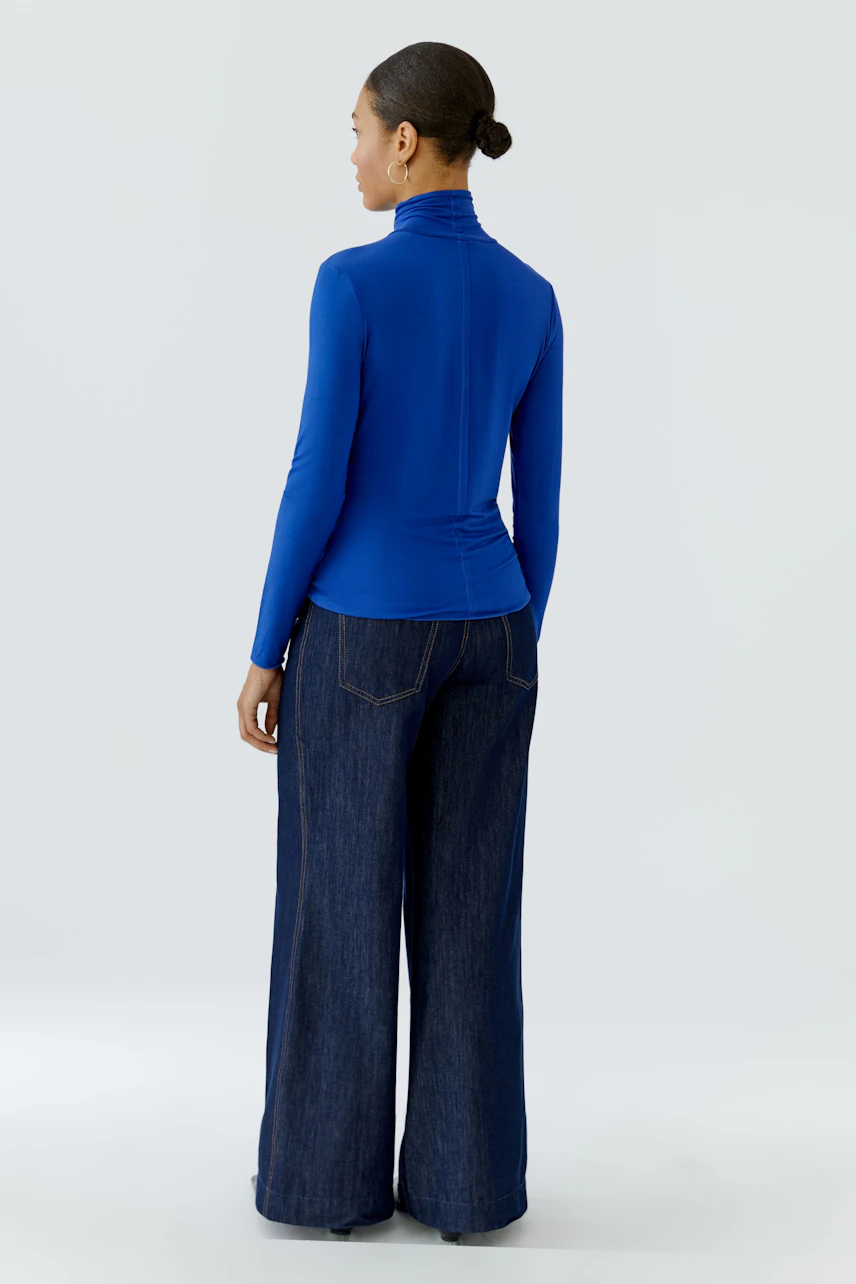 Woman in blue long-sleeve shirt and wide-leg jeans, viewed from the back.