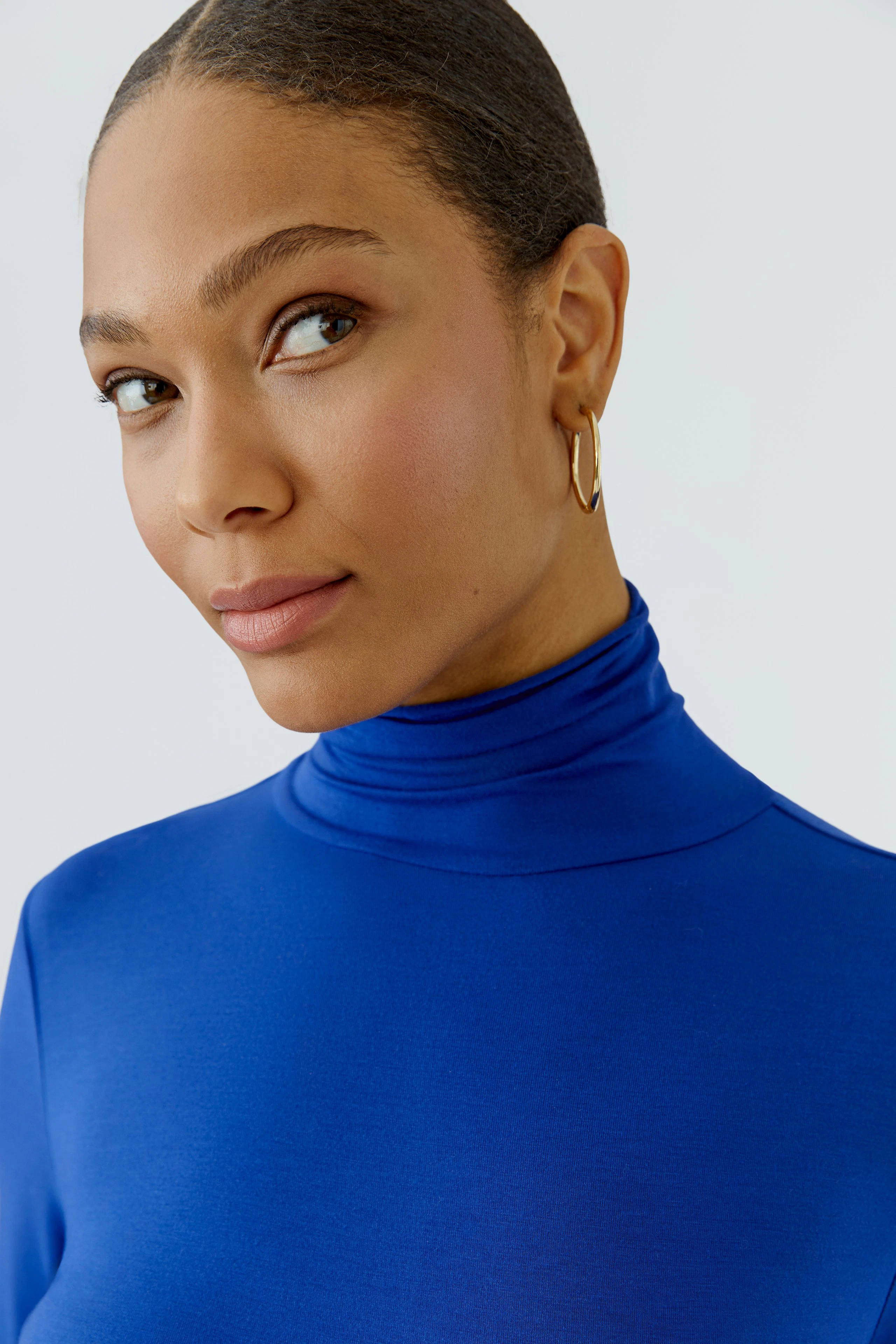 Woman in a blue long-sleeve shirt with a turtleneck, looking confidently to the side.