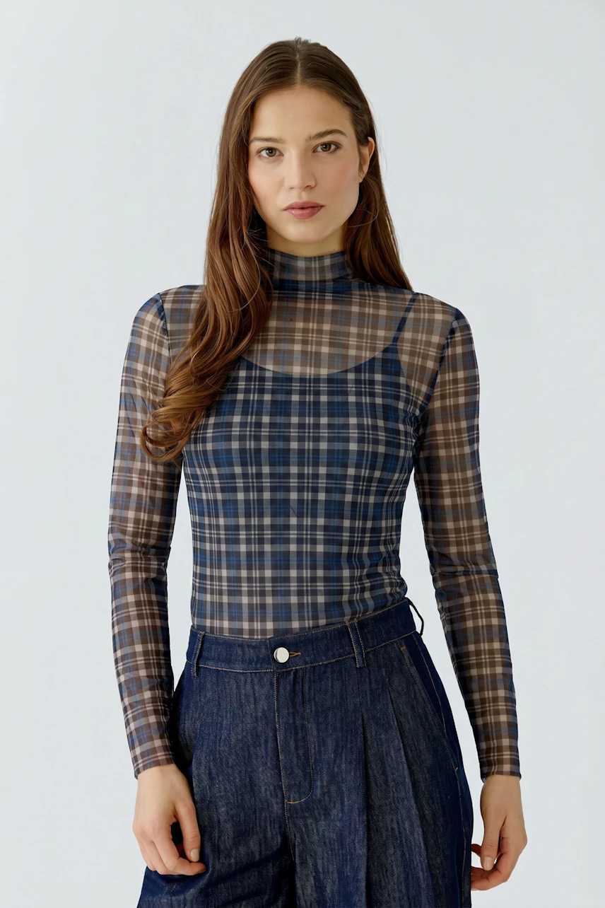 Casual women's long-sleeve shirt: Woman in plaid shirt and denim pants, looking confidently.