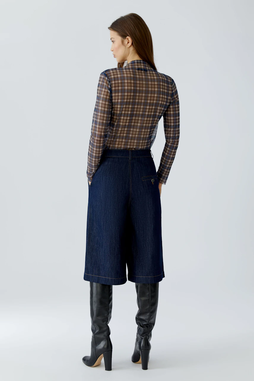Casual long-sleeve shirt: Woman in plaid shirt, denim culottes, and knee-high boots, facing away.