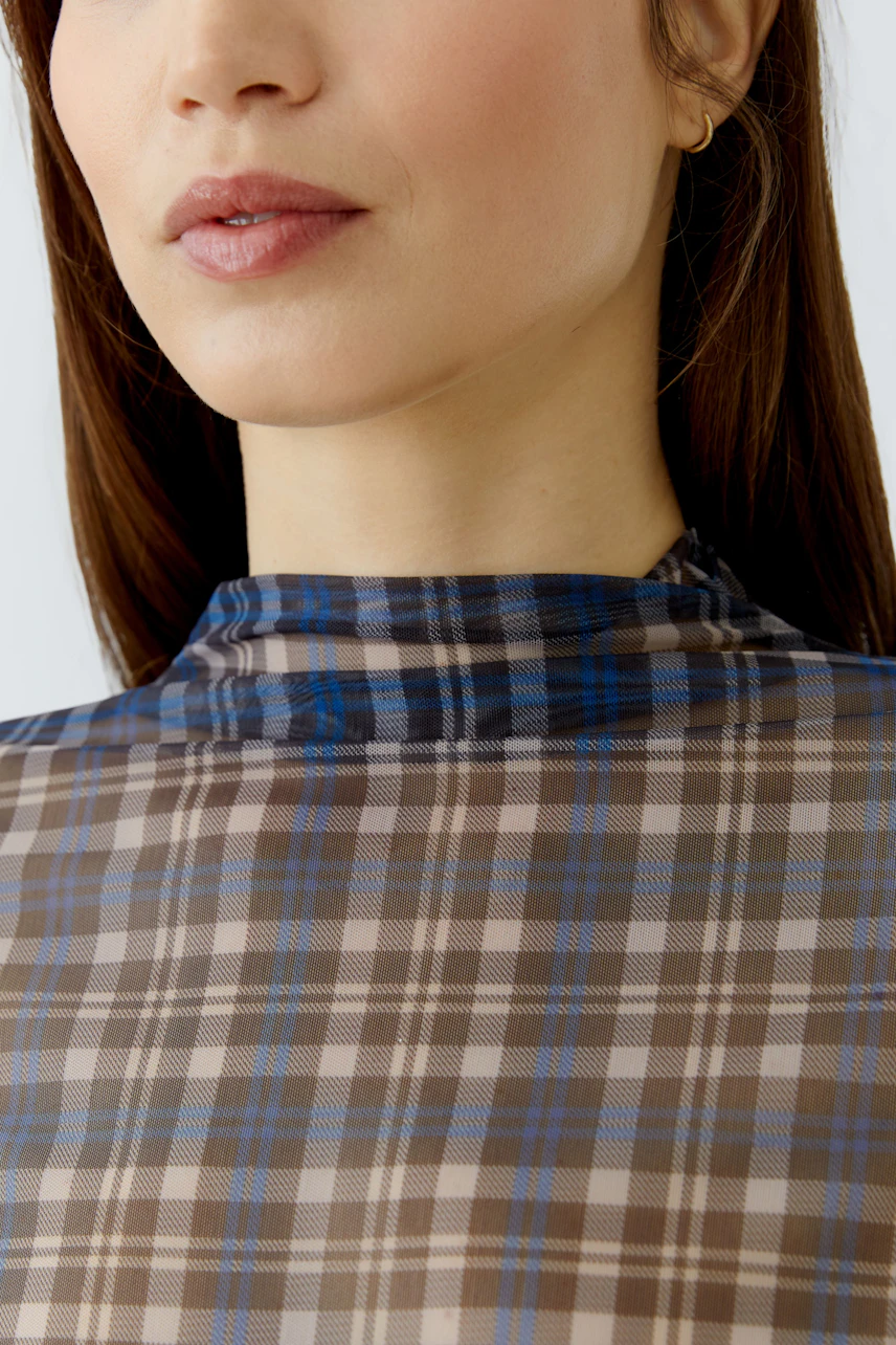 Woman in plaid long-sleeve shirt with high neck, showcasing modern style.