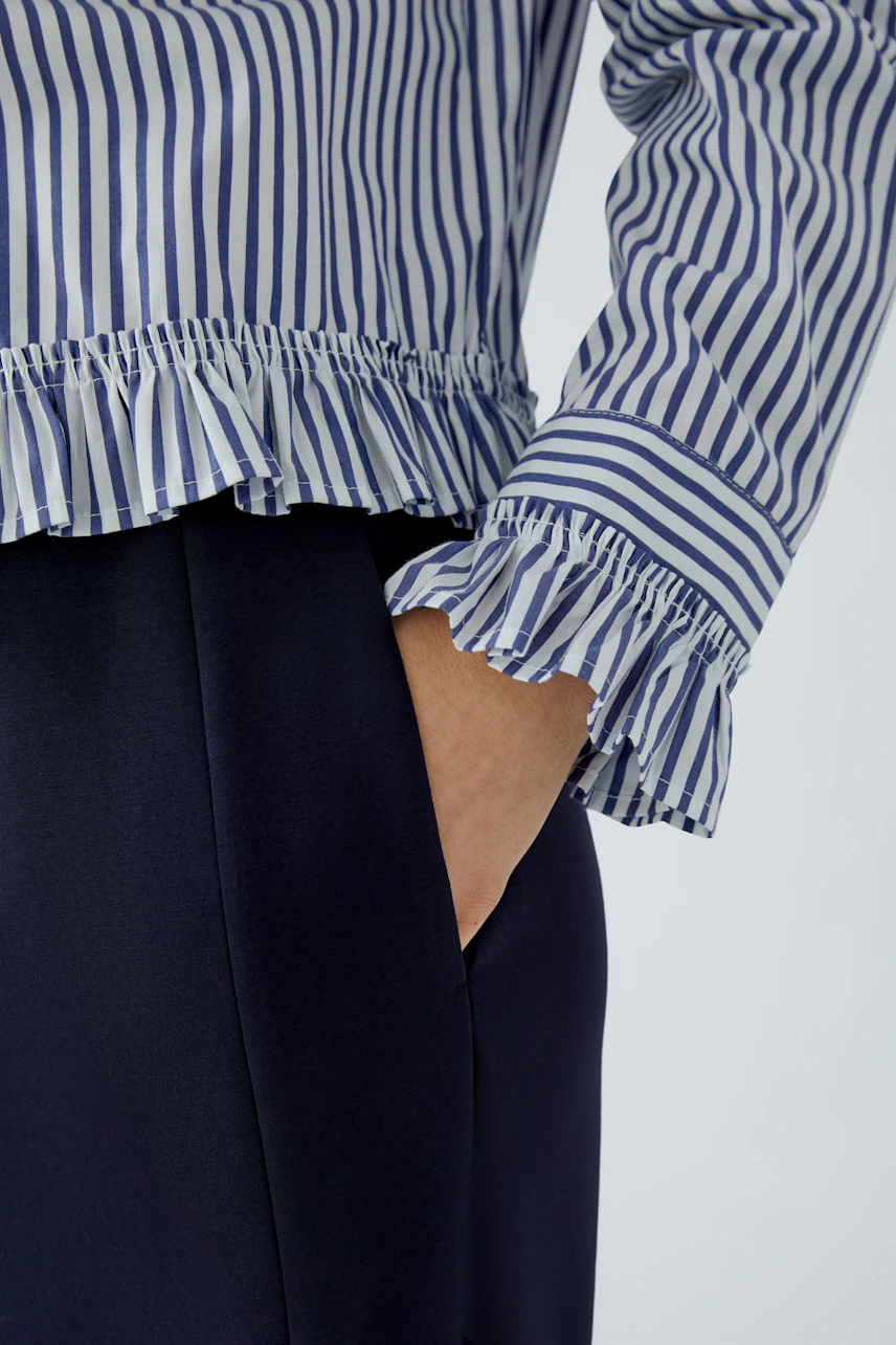 Gestreifte Hemdbluse mit Rüschenärmeln, kombiniert mit dunkler Hose. Keine Frau im Bild.