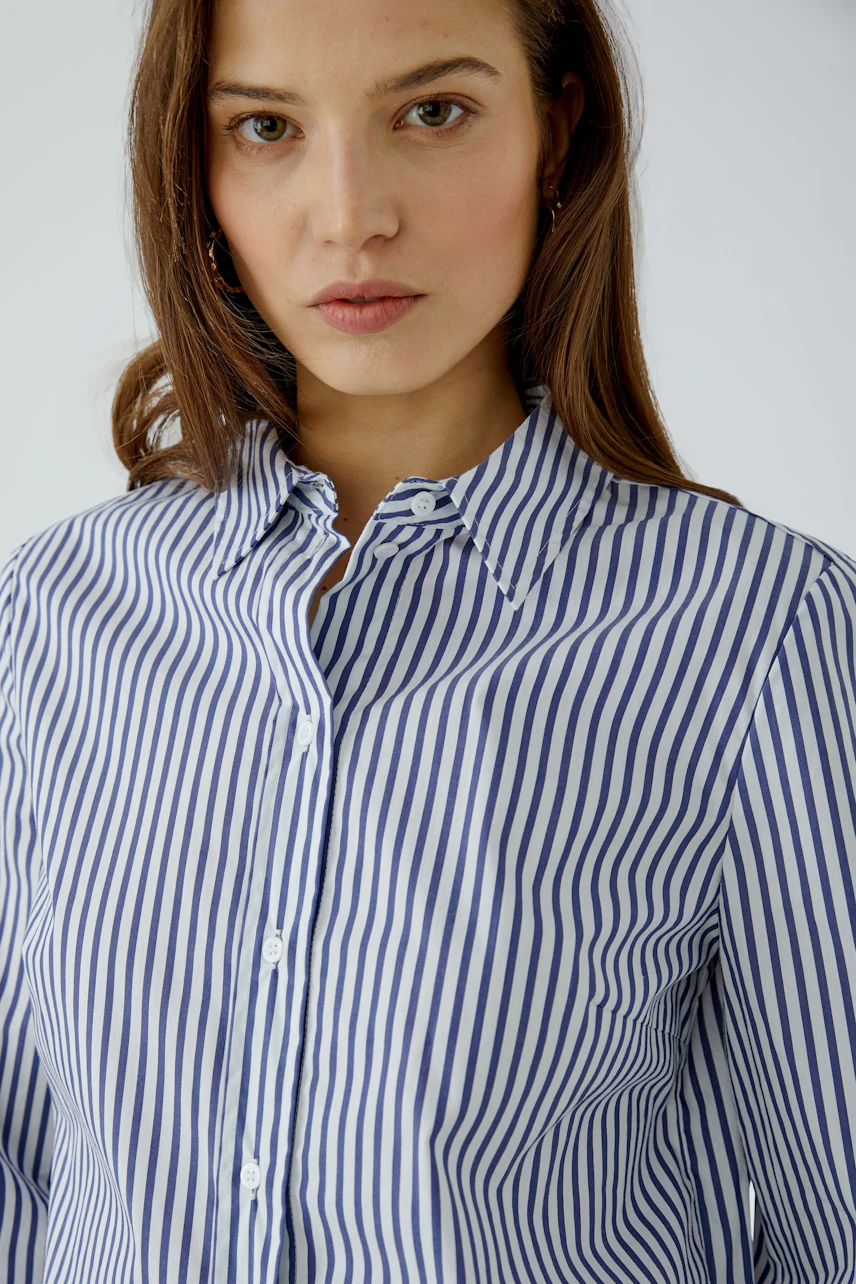 Gestreifte Hemdbluse: Frau in blau-weiß gestreifter Bluse mit offenem Kragen, lässiger Look.