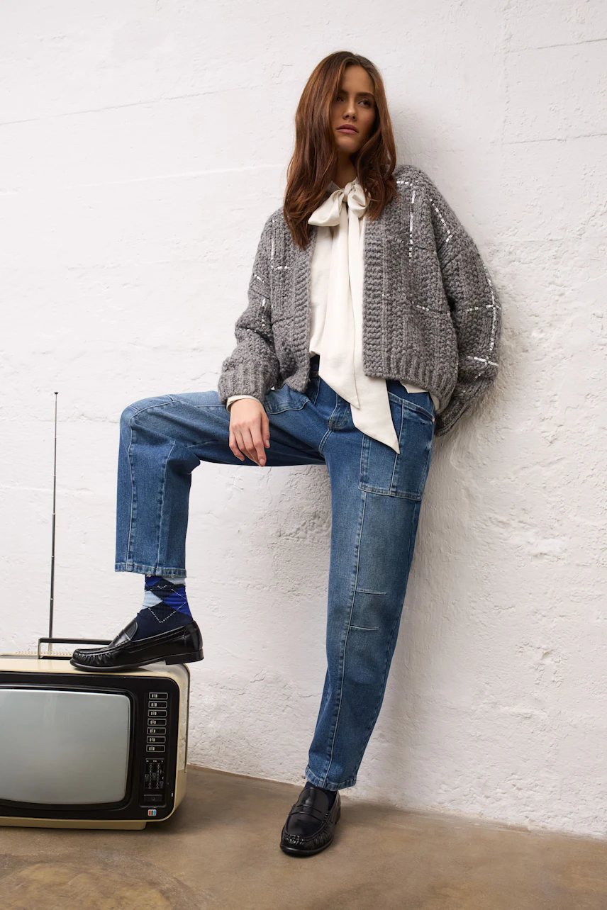 Frau in Jeans Barrel und lila Pullover, lässig sitzend. Kombiniert mit gestreifter Bluse und Socken.