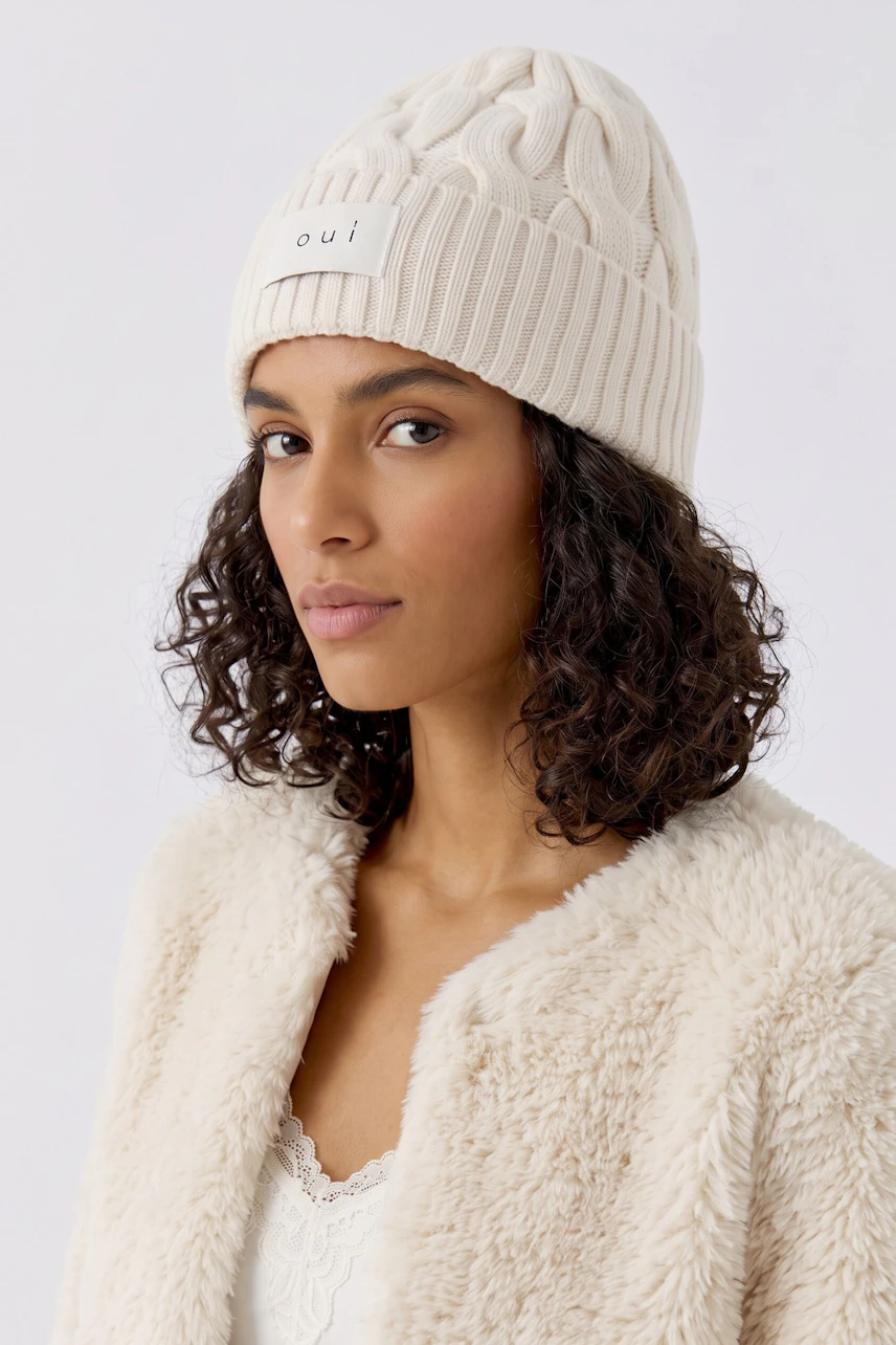Woman in a cozy knit hat, cream color, with a textured pattern, paired with a green jacket.