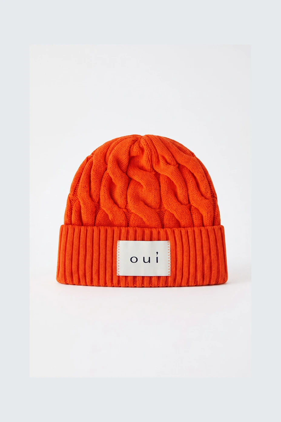 Bright orange knit beanie with ribbed cuff and 'oui' logo patch.