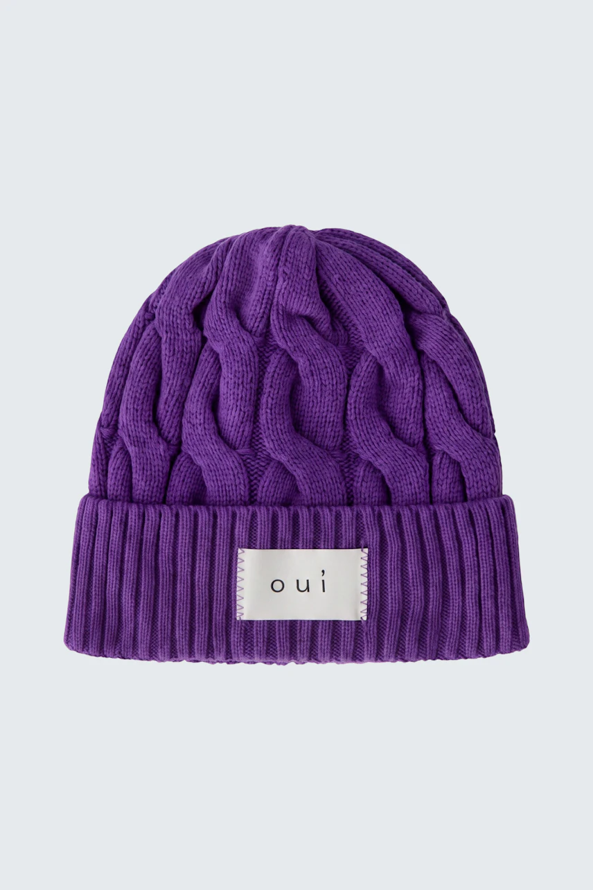 Lila Strickmütze von Oui mit Zopfmuster und Logo-Patch, ideal für kalte Tage.