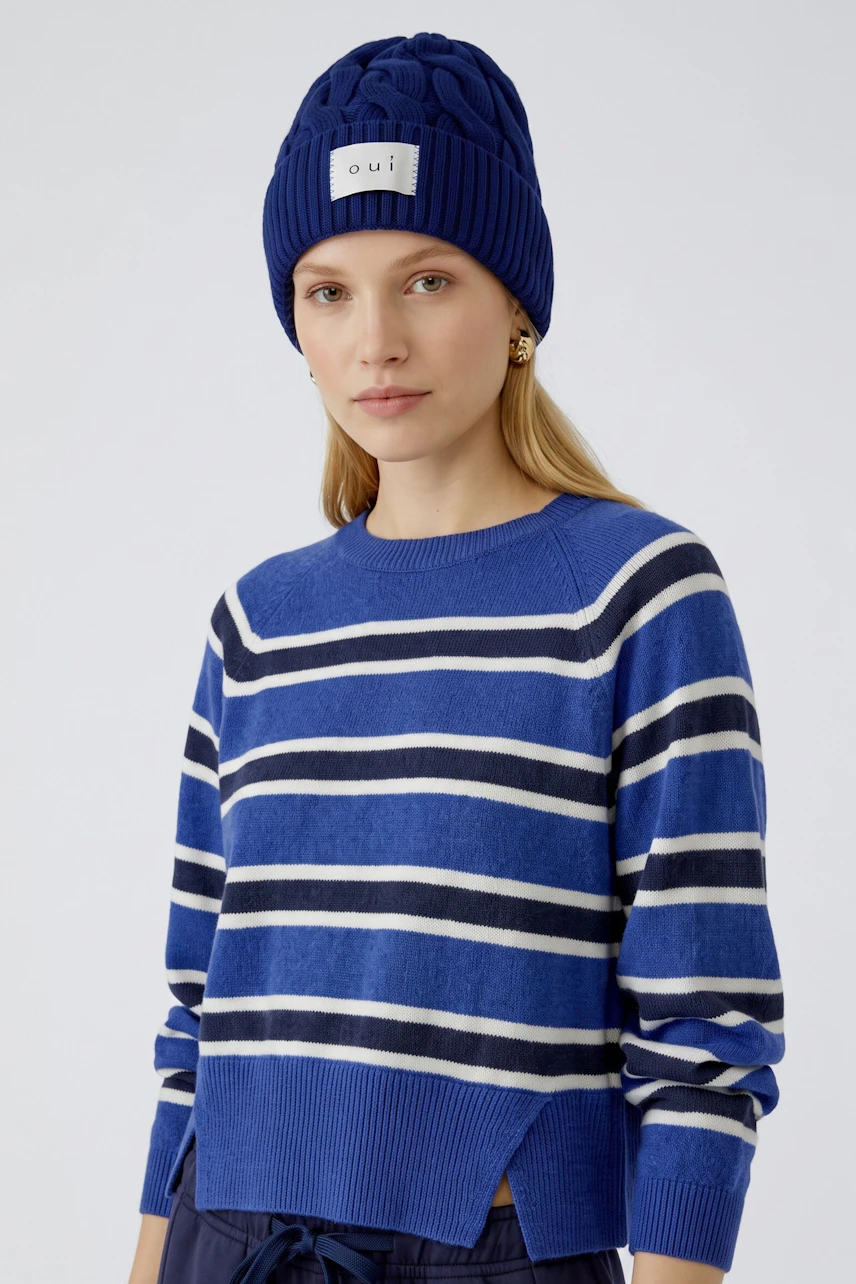 Frau mit blauer Mütze von Oui, lässiger Pullover und Jeans. Schlichtes, modernes Design.
