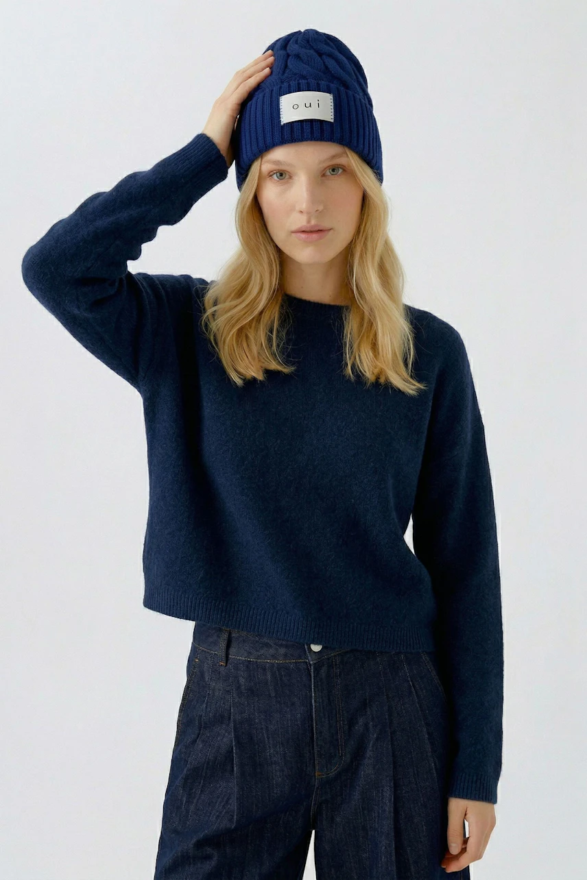 Frau mit blauer Mütze von Oui, lässiger Pullover und Jeans. Schlichtes, modernes Design.