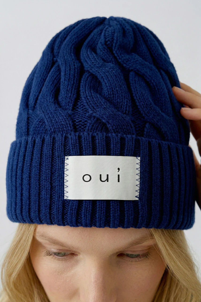 Blaue Strickmütze: Frau trägt eine warme, grob gestrickte Mütze mit Oui-Logo, ideal für kalte Tage.