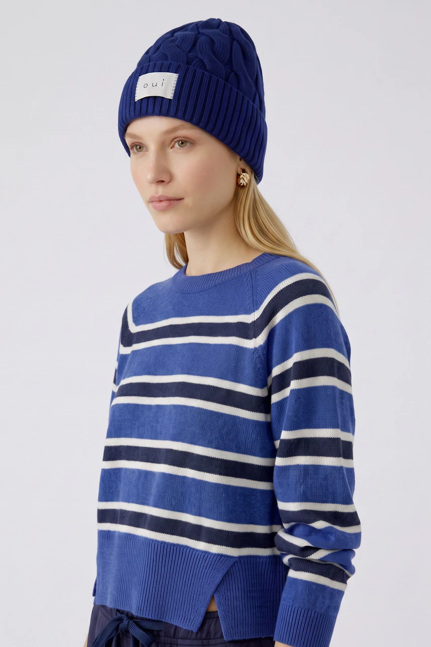 Blaue Strickmütze: Frau trägt eine warme, grob gestrickte Mütze mit Oui-Logo, ideal für kalte Tage.
