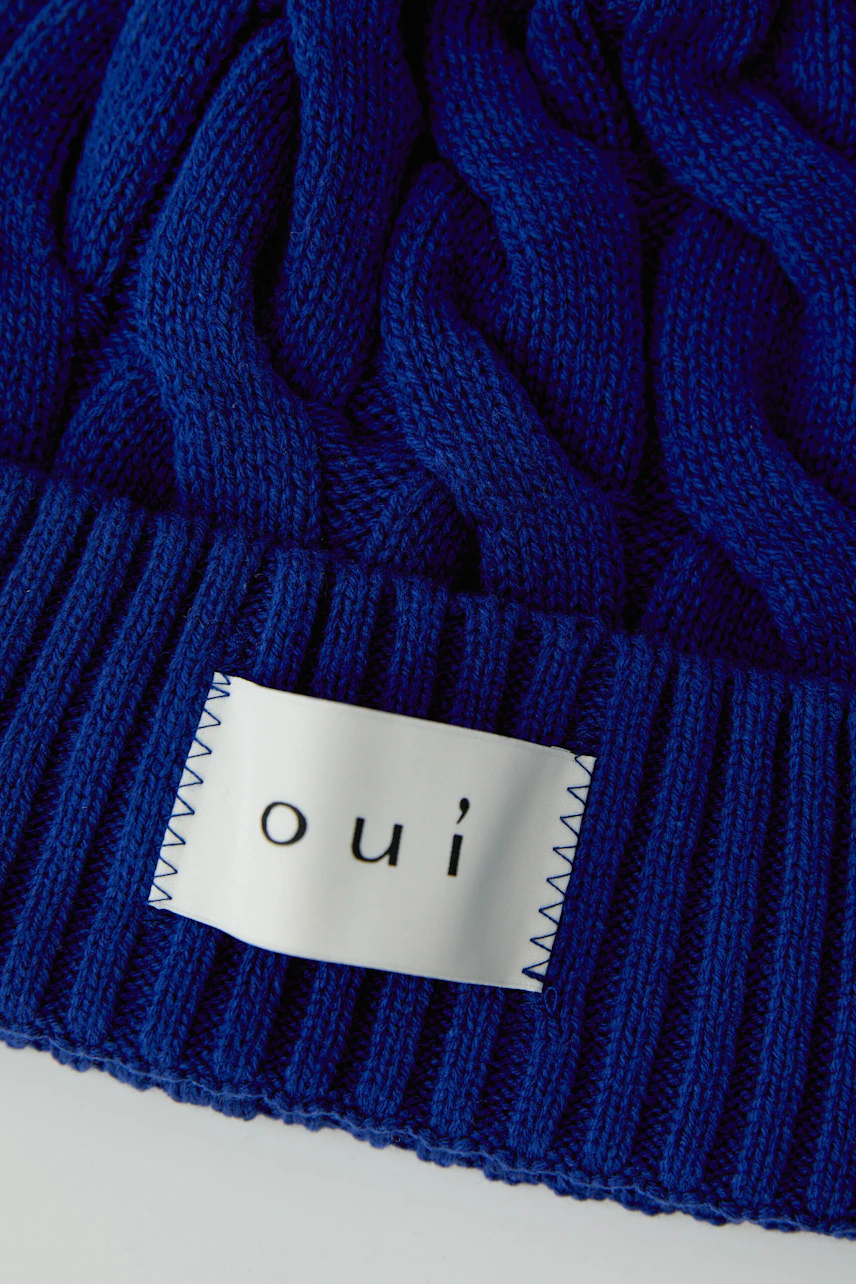 Blaue Strickmütze von Oui mit Zopfmuster und Label-Detail, ideal für kalte Tage.