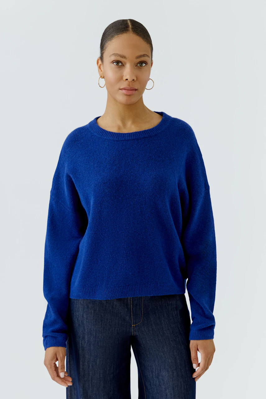 Frau im blauen Pullover: Lässiger Strickpullover kombiniert mit dunkler Jeans, schlicht und modern.