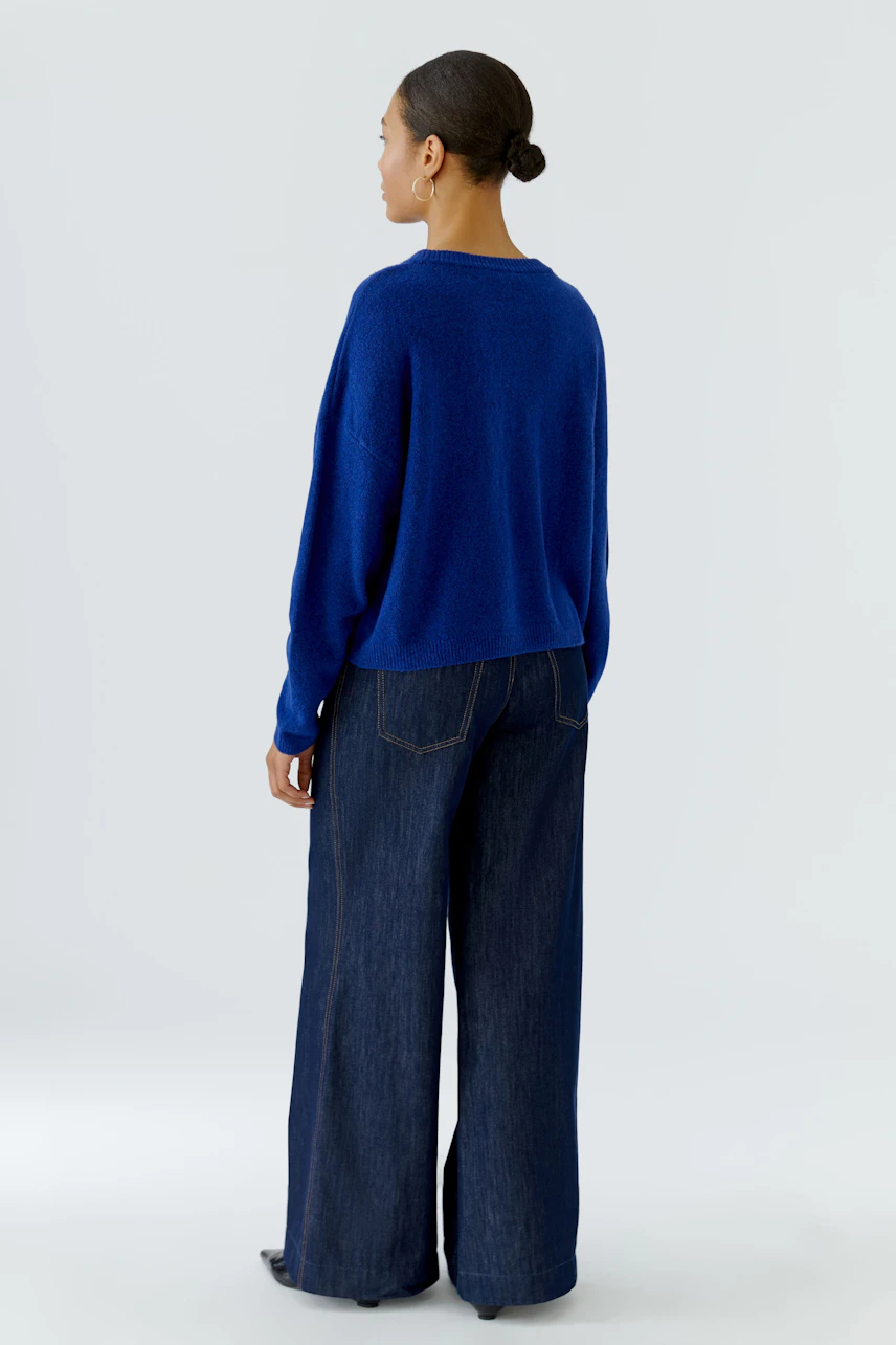 Frau im blauen Pullover und weiten Jeans, von hinten gesehen. Lässiger Look für den Alltag.