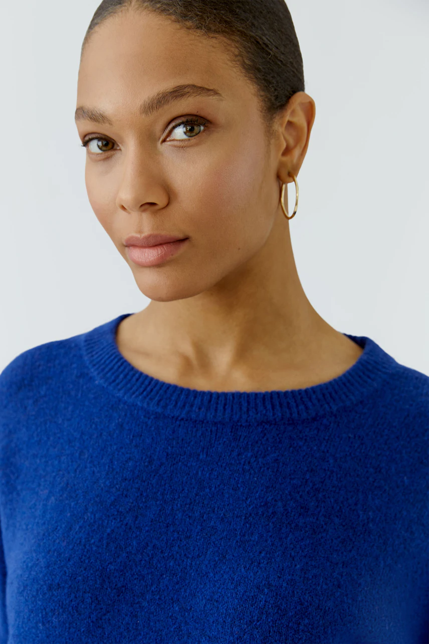 Frau im blauen Pullover mit Rundhalsausschnitt, schlicht und modern.
