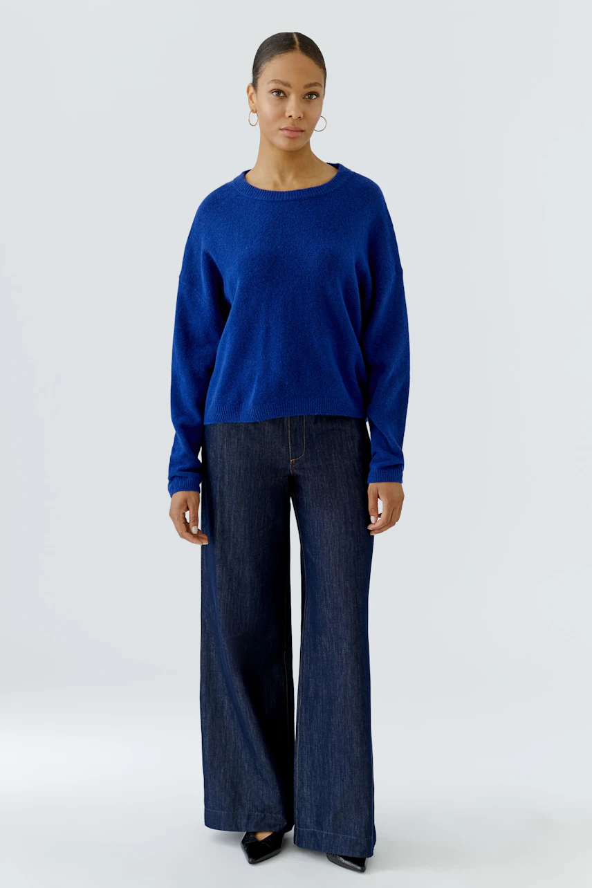 Frau im blauen Pullover und weiter Jeans, schlicht und modern.