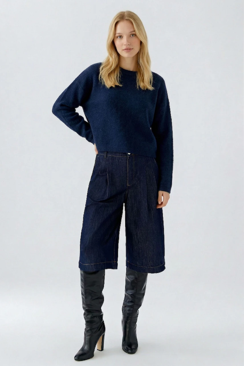 Casual women's pullover: Woman in a navy pullover with wide-leg jeans and knee-high boots, standing confidently.