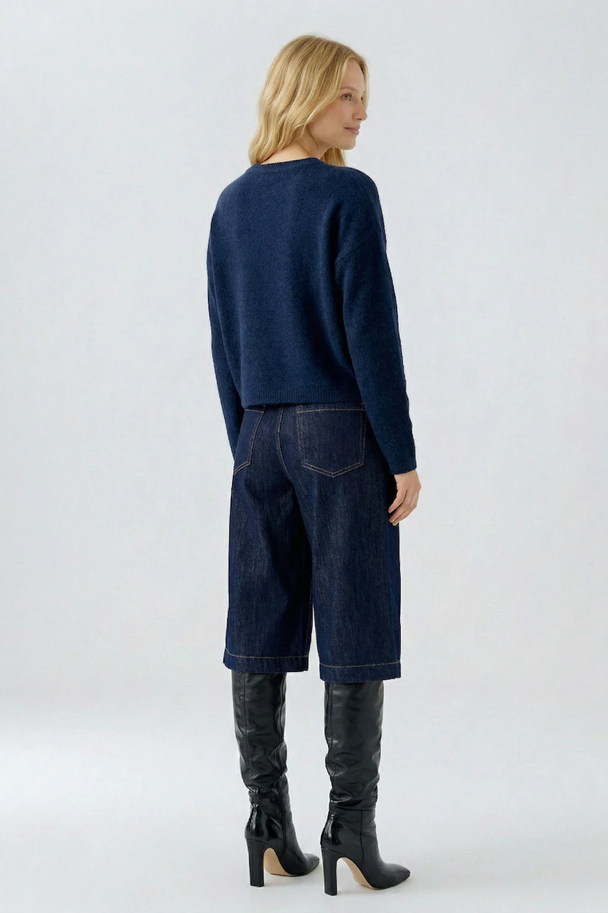 Casual pullover: Woman in a navy pullover with wide-leg jeans and knee-high boots, facing away.