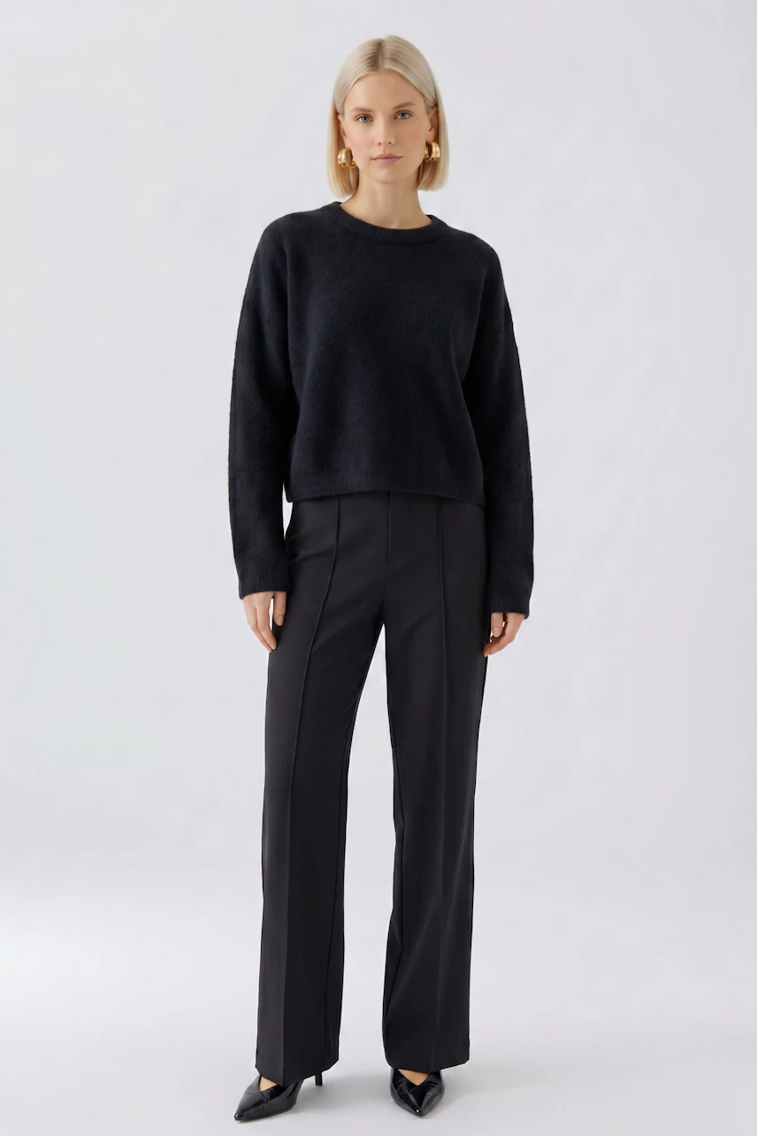 Frau im schwarzen Pullover und dunkler Hose, schlicht und modern, mit goldenen Ohrringen.