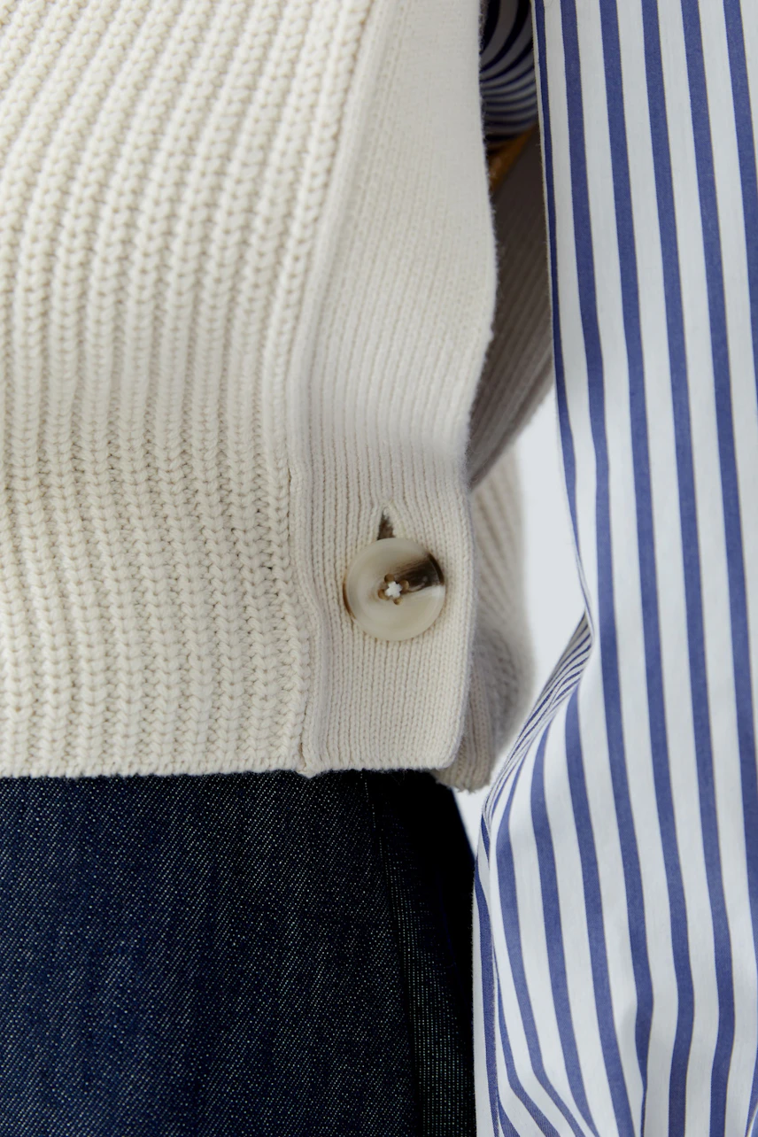 Casual women's pullover vest: Cream knit with side button detail over striped shirt and denim.