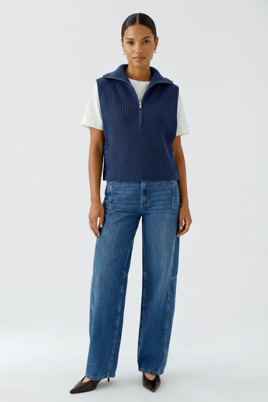 Casual women's pullover: Woman in a navy sleeveless pullover over a white tee, paired with blue jeans.